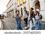 Four happy tourists with backpacks are walking and crossing the street in lisbon near a tram, a man is pointing his finger showing something to his friends