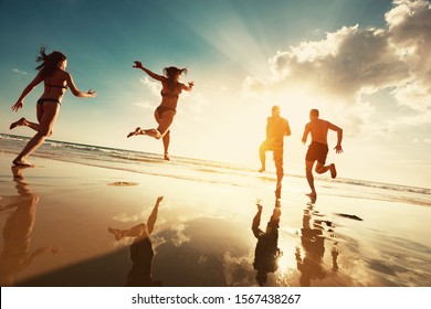 Four Happy Tourists Runs To Sunset Sea Beach. Beach Vacations Concept