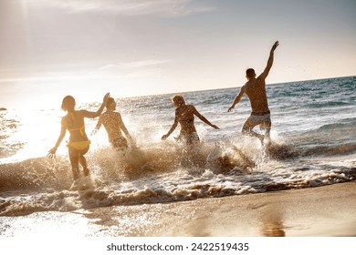 Four happy young friends or tourists are having fun, runs and jumps at sunset sea beach. Tropical vacations concept - Powered by Shutterstock