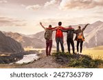 Four happy young tourists with backpacks are standing and embracing in mountains and enjoying sunset