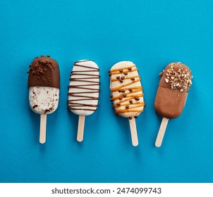 Four ice creams with chocolate glaze on sticks on blue background.