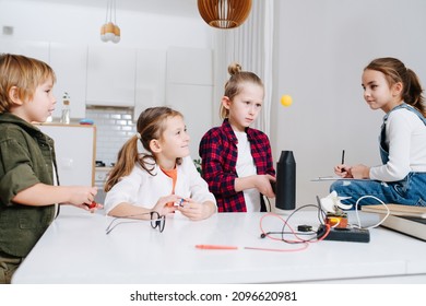 Four Kids Doing Home Science Project, Hovering Ping Pong Ball With A Fan, Girl Is Documenting The Process. All Behind The Table.