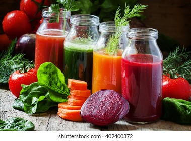 Four kind of vegetable juices: red, burgundy, orange, green, in small glass bottles, fresh vegetables and herbs, vintage wooden background, selective focus