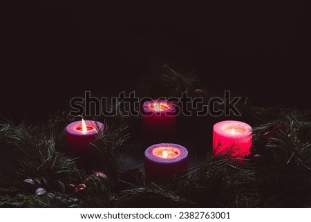 Four lit advent candles in an advent wreath in a dark room with copy space