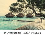 A four luxury resort bungalows surrounded by a beautiful turquoise ocean water of a Maldives resort; a row of several luxurious hotel cottages with triangle roofs, wooden pier, and breaking teal waves