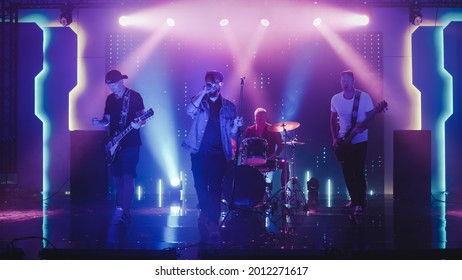 Four Man Rock Band with Lead Singer, Guitarists, Bassist and Drummer Performing at a Concert in a Night Club. Live Music Party in Front of Bright Colorful Strobing Lights on Stage. - Powered by Shutterstock