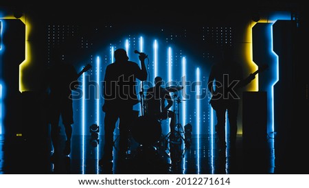 Four Man Rock Band with Lead Singer, Guitarists, Bassist and Drummer Performing at a Concert in a Night Club. Live Music Party in Front of Bright Colorful Strobing Lights on Stage.