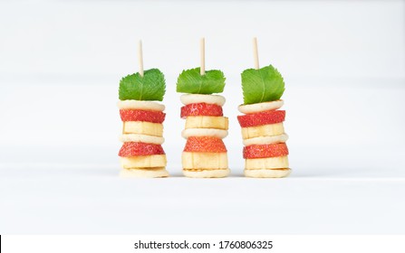 Four Mini Pancakes On A Skewer With A Mini Banana, Strawberries And Fresh Green Mint On White Background