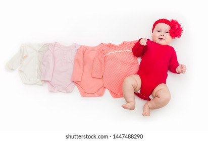 A Four Month Happy Baby In Red Bodysuit Lying On A White Background With Pink Clothes Smaller Size.