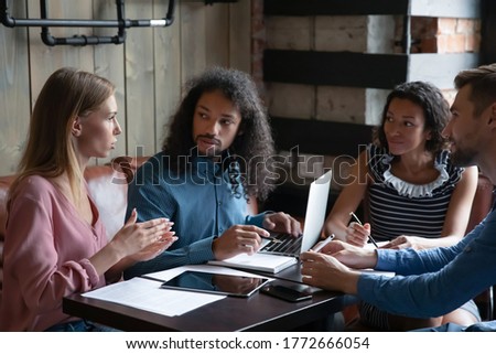 Four multi ethnic young group of employees during lunch in cafe working together on common project, corporate task, preparing for conference activity, listen team leader. Mentoring, teamwork concept