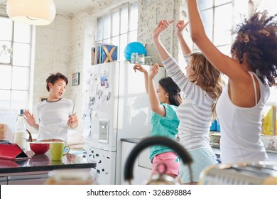 Four Multi Racial Girl Friends In Kitchen At Home Wearing Pajamas Dancing Wildly Arms In Air Copying Moves Swinging Hips