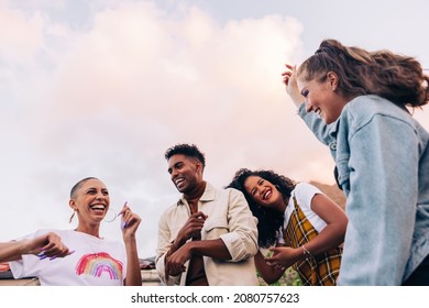 Four multicultural friends dancing on the rooftop. Group of happy young friends laughing and having a good time during a party. Vibrant young people having fun together on the weekend.