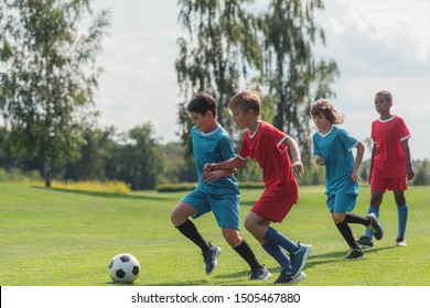 Four Multicultural Kids Playing Football On Grass  