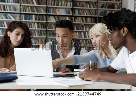 Four multiethnic schoolmates look at laptop discuss online task, learning use internet resources, search information busy in studying sit at table in university library. Higher education, tech concept
