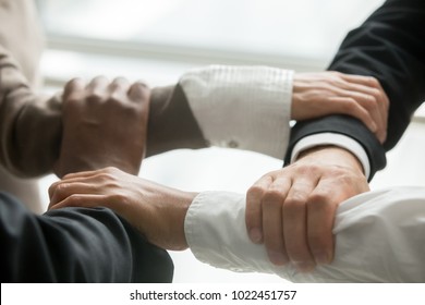 Four multiracial business people holding each others wrists, diverse partners join hands together as concept of reliable support in team, strength, power and unity in collaboration, close up view