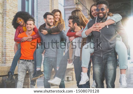 Four multiracial couples having fun piggybacking under the city arcades in the morning. Students having fun in the city.
