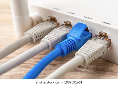 Four network cable plugs connected to the white Wi-Fi wireless router on a wooden desk. Macro shot of home and office wlan router provides an internet connection. Internet hardware device. Close-up.