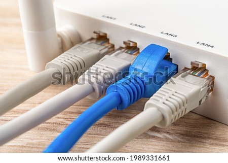 Four network cable plugs connected to the white Wi-Fi wireless router on a wooden desk. Macro shot of home and office wlan router provides an internet connection. Internet hardware device. Close-up.