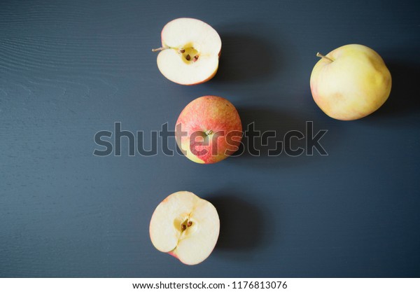 Four nice and delicious apples on a gray\
surface top view. One of these sweet desserts is cut into two\
parts. Bright and colorful background.\
