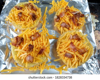 Four Open Buns Covered With Shredded Cheddar Cheese Topped With Cooked Bacon Pieces. Top View Of Buns On Foil Ready To Cook Or Broil