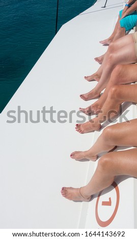 Four pairs of bare legs of female tourists sat on a boat.Sea is visible.Vertical Image