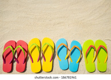 Four Pairs Of Beach Sandals On White Sand