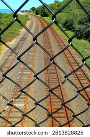 Four parallel sets of rusty railroad tracks as seen through wire fencing stretch out toward a distant horizon.