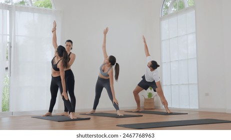 Four people in a bright, modern studio practicing seated forward bend poses with an instructor providing assistance. Group yoga class featuring diverse participants. - Powered by Shutterstock