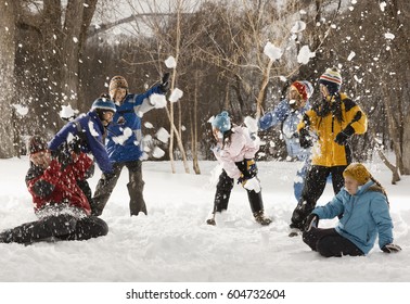 Four people outdors in hats, coats and scarves, having an energetic snowball fight,
