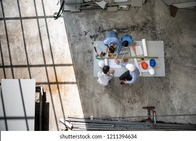 Four Persons Professional Team Of Engineers Talk Together To Review Material In Construction Site, Taken From Above High Angle, Top View Photo With Shadow Of Window Frame On Floor.