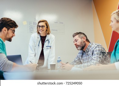 Four Physicians In Meeting At Hospital Boardroom. Hospital Staff Meeting In Conference Room.