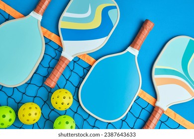 four pickleball paddles in blue tones on top of a net on a blue background with three balls next to it