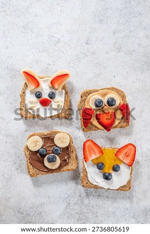 Four pieces of bread show fun animal faces made with different fruits and spreads. The bread is laid out on a table in a kitchen. This activity is great for kids and family moments.