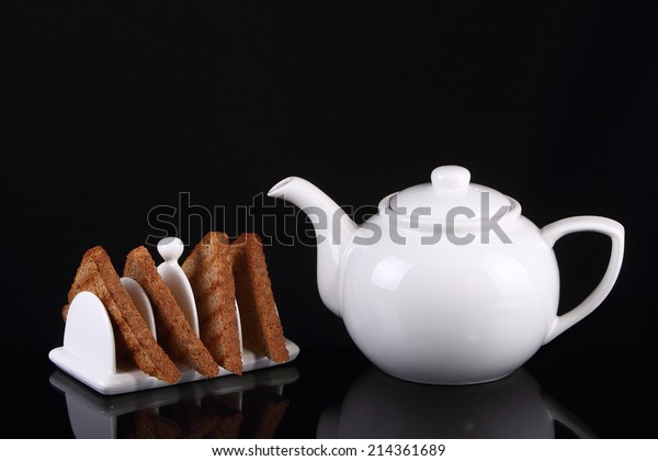 Four pieces of toast in a porcelain toast rack\
with white porcelain\
teapot.