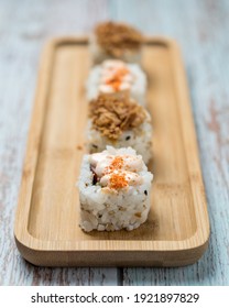 Four Pieces Of Uramaki Sushi On A Wood Plate