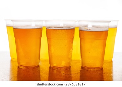 Four plastic glasses of frothy beer on a wooden table with a white backdrop. - Powered by Shutterstock