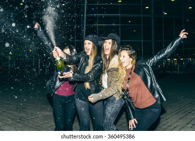 Four pretty girl celebrating something outdoors - Women opening and sprinkling a white wine bottle - Group of friends having fun, frontal flash added to give realism to the photo - Powered by Shutterstock