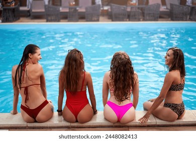 Four pretty girls in wet colorful bikini talk, chill sitting by the swimming pool in a row. Fit slender women in swimwear gossip, chat. Females relax on poolside summer party in hotel at night. - Powered by Shutterstock