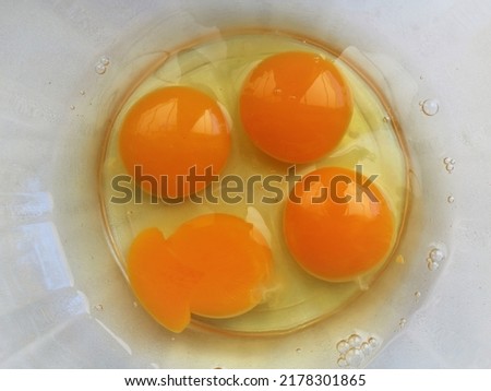 four raw chicken eggs broken into a transparent glass bowl standing on a white table top view, food protein ingredients of animal origin, homemade breakfast products