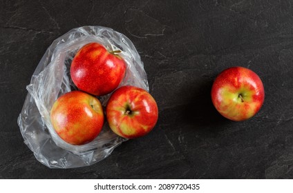 Four Red Apples With Plastic Bag From Supermarket On Black Slate Like Table, View From Above