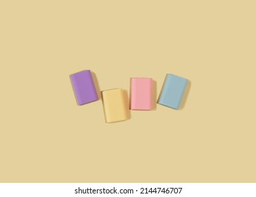 Four rubber erasers in pastel colors on a light yellow background. National rubber eraser day concept. Top view, flat lay.