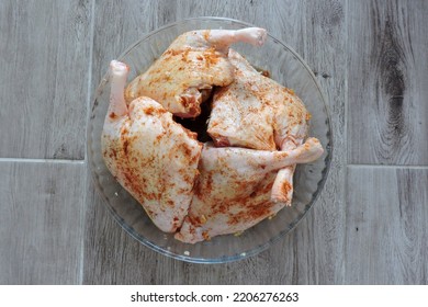 Four Seasoned Raw Whole Chicken Legs In A Glass Heat-resistant Vessel, The Grey Wooden Background