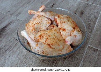 Four Seasoned Raw Whole Chicken Legs In A Glass Heat-resistant Vessel, The Grey Wooden Background