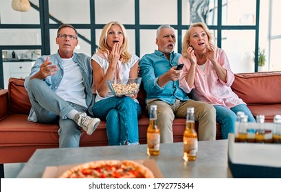 Four senior friends having fun at home.  Group of old friends watching TV in modern apartment. Two handsome mature men and two attractive women spending time together indoors. - Shutterstock ID 1792775344