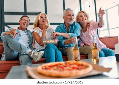 Four Senior Friends Having Fun At Home.  Group Of Old Friends Watching TV In Modern Apartment. Two Handsome Mature Men And Two Attractive Women Spending Time Together Indoors.