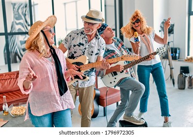 Four Senior Friends Having Fun At Home.  Group Of Old Friends Singing And Playing Guitars In Modern Apartment. Two Handsome Men And Two Women Spending Time Together Indoors. Improvised Rock Band.