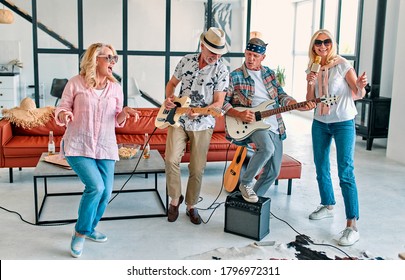 Four Senior Friends Having Fun At Home.  Group Of Old Friends Singing And Playing Guitars In Modern Apartment. Two Handsome Men And Two Women Spending Time Together Indoors. Improvised Rock Band.