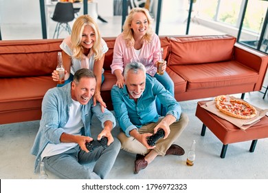 Four senior friends having fun at home.  Group of old friends playing video games in modern apartment. Two handsome mature men and two attractive women spending time together indoors. - Powered by Shutterstock