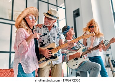 Four Senior Friends Having Fun At Home.  Group Of Old Friends Singing And Playing Guitars In Modern Apartment. Two Handsome Men And Two Women Spending Time Together Indoors. Improvised Rock Band.