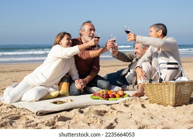 Four senior friends having picnic at beach on sunny day, raising glasses of red wine and pronouncing toast. Two middle-aged couples clinking glasses, celebrating outside. Celebration, leisure concept - Powered by Shutterstock